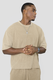 A man wearing a beige oversized t-shirt with 'FOYERADI' printed on the chest, paired with matching beige drawstring pants, against a solid light gray background.