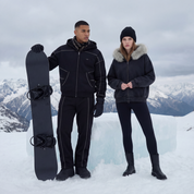 Two people in winter clothing standing on a snowy mountain with a snowboard.