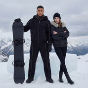 Two people standing in the snow with a snowboard, wearing winter clothing.
