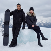 Two people in winter clothing with a snowboard on a snowy mountain