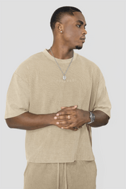 A man wearing a beige oversized t-shirt with 'FOYERADI' printed on the chest, paired with matching beige drawstring pants, against a solid light gray background.